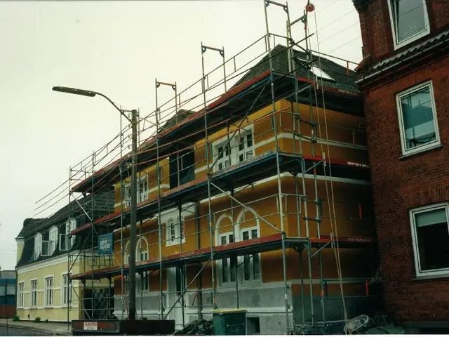 The image shows a building with scaffolding on the side of it, surrounded by street poles, street...