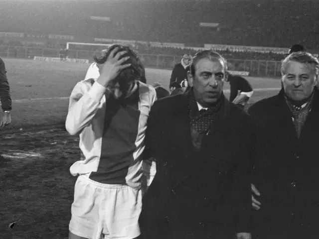 The image shows a group of men standing next to each other on top of a soccer field, with a stadium...