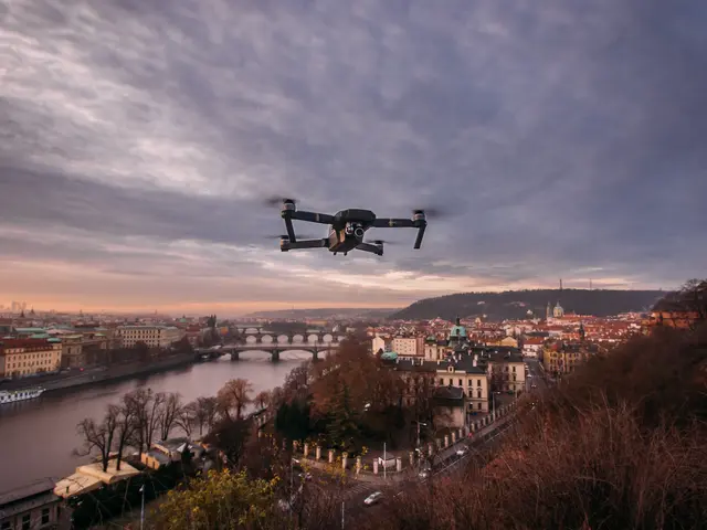 The image shows a drone flying over a city with a river in the background. The city is filled with...