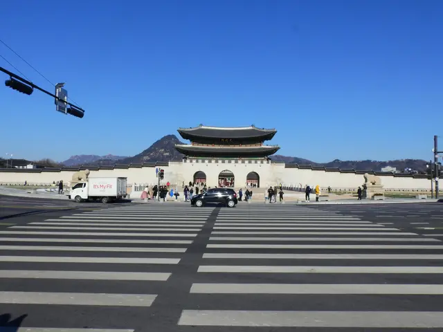 The image shows a group of people standing on the ground in front of Gyeongbokgung Palace in Seoul,...