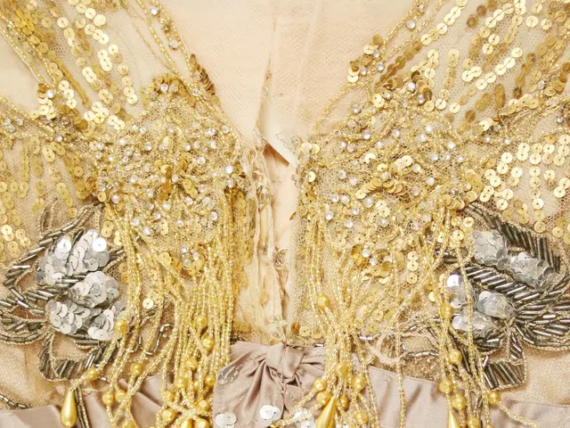 The image shows a close up of a dress with gold sequins and pearls adorning it. The dress is a...