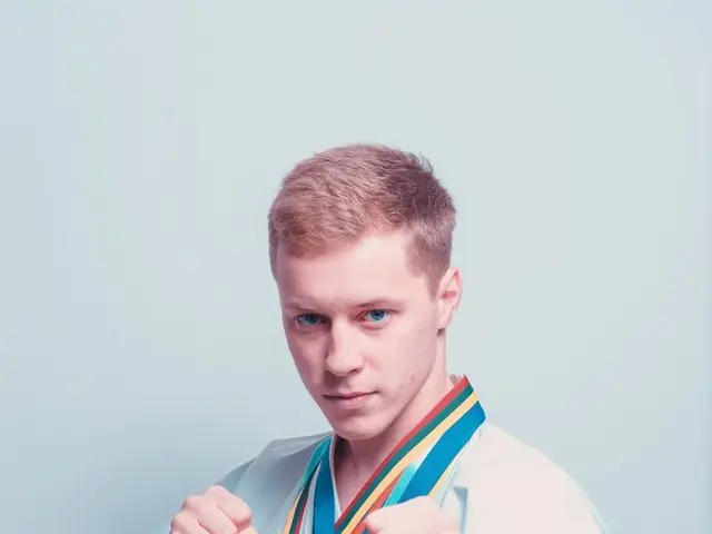 The image shows a young man in a karate kimono with medals around his neck, standing in front of a...