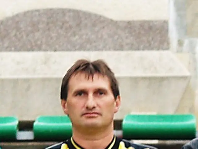 The image shows a man in a yellow shirt standing next to another man wearing a black jacket. In the...