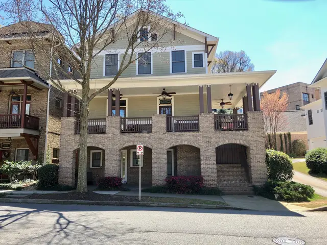 The image shows a two story apartment building with a car parked in front of it, surrounded by...