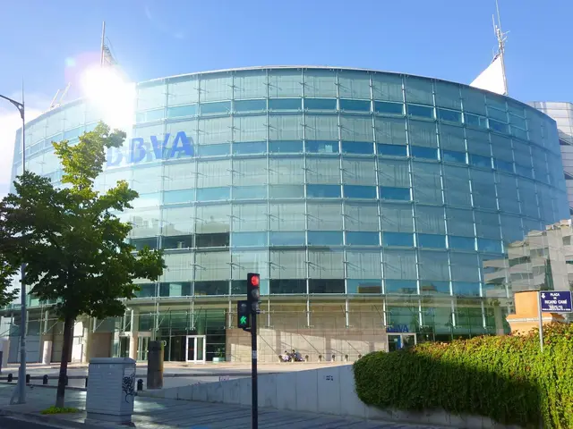 The image shows a large glass building with a lot of windows on the side of it, surrounded by...