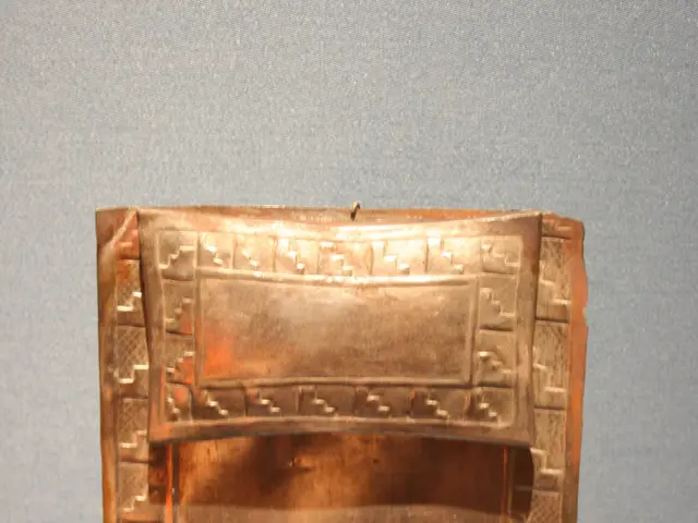 The image shows a copper plaque on display in a museum, with a wall in the background and a number...