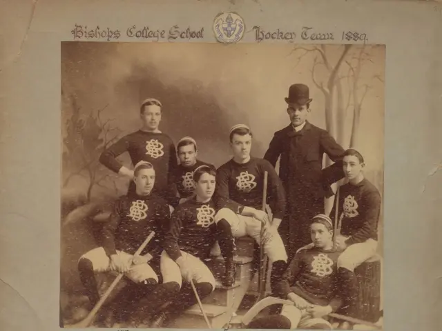 The image shows an old photo of a hockey team posing for a picture. There are a few people sitting...