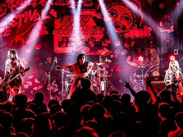 The image shows a group of people on stage playing guitars and singing, with mics and stands set up...