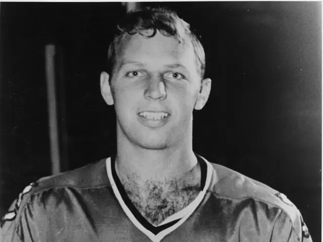 The image shows a black and white photo of a hockey player wearing a jersey with a smile on his...