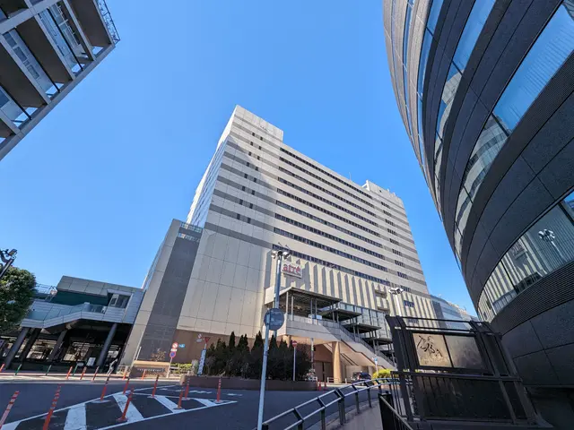 The image shows a tall building with many windows in the middle of a city, surrounded by street...