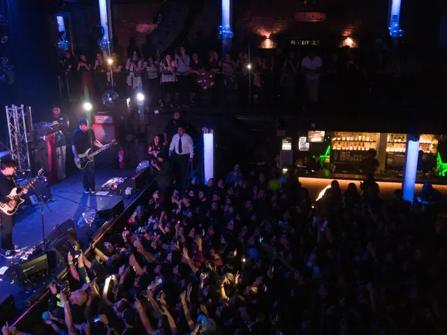 The image shows a band performing on stage at a concert in front of a large crowd. We can see the...