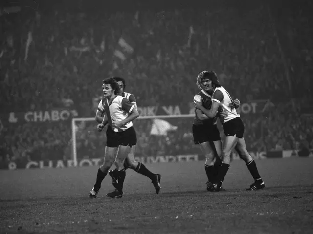 The image shows a group of men playing a game of rugby on a field, with a net in the background and...