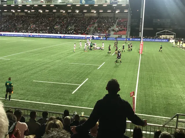 The image shows a group of people playing a game of rugby in a stadium. The stadium is filled with...