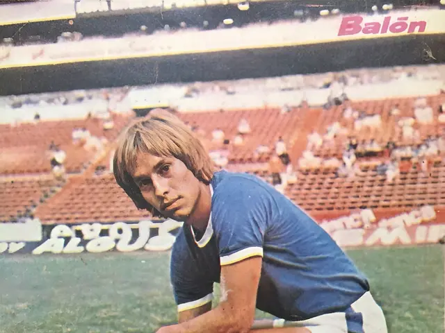 The image shows a man kneeling on top of a soccer field, surrounded by a group of people sitting on...