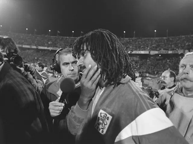 The image shows a man with dreadlocks talking to a reporter in front of a crowd. He is wearing a...