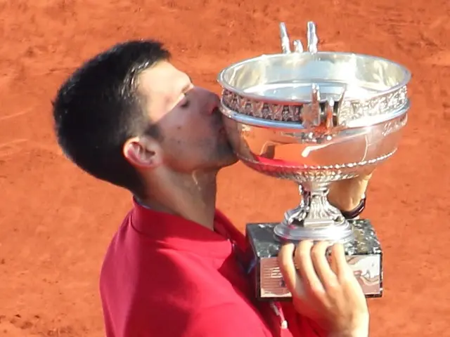 The image shows Novak Djokovic of Serbia celebrating with the French Open trophy after defeating...