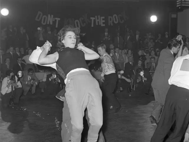 The image shows a group of people dancing on a dance floor in front of a crowd of people sitting...