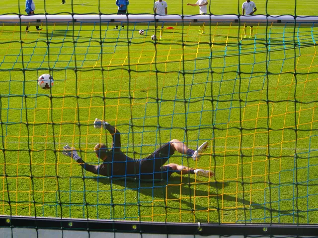 The image shows a soccer player making a save in front of a goal, with a net in the foreground and...