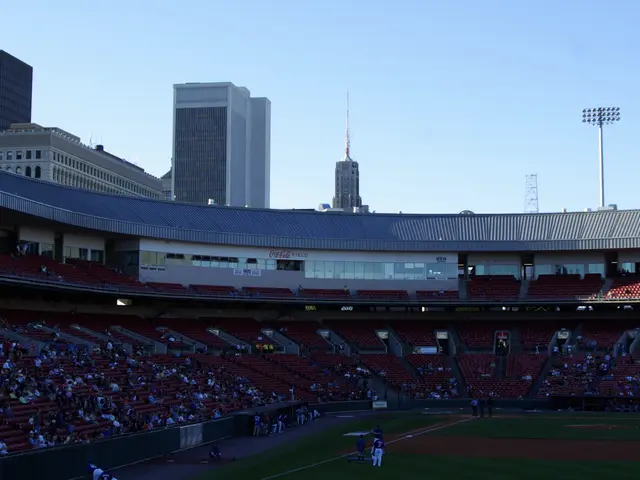 The image shows a baseball stadium filled with lots of people watching a game. On the ground, there...