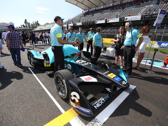 The image shows a group of people standing around a race car on a track, with a stadium in the...