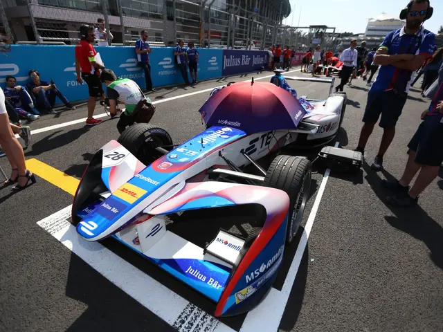 The image shows a Formula E car parked on the side of a race track, surrounded by a group of...