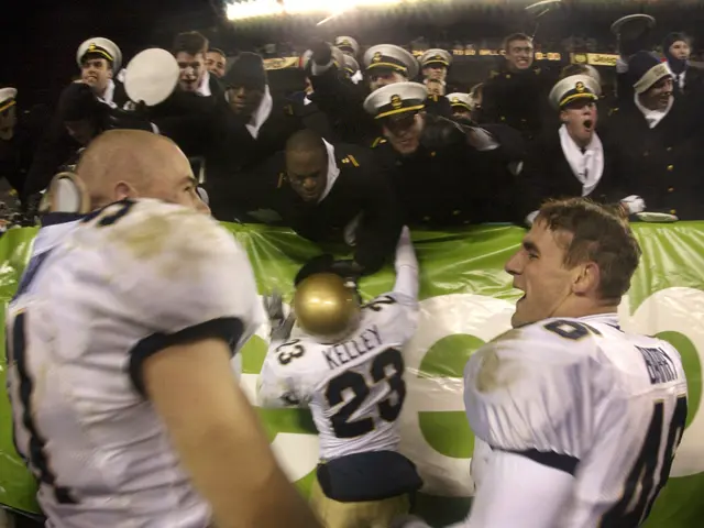 The image shows a group of men standing on top of a football field, wearing caps and holding a...