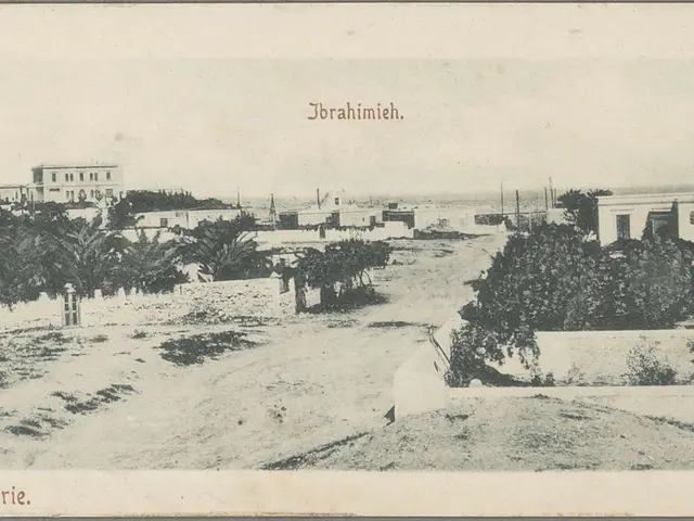 The image shows an old black and white photo of a dirt road with trees and buildings in the...