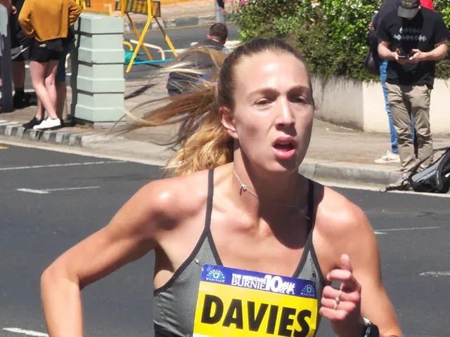 The image shows a woman running in a marathon wearing a sports bra top and shorts. She is...