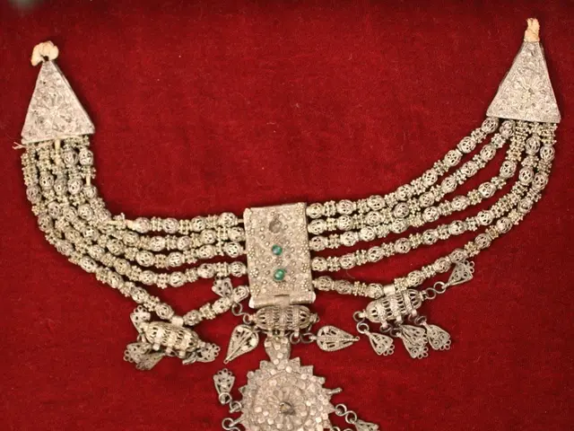 The image shows a silver necklace with emeralds and diamonds on a red velvet background. The...
