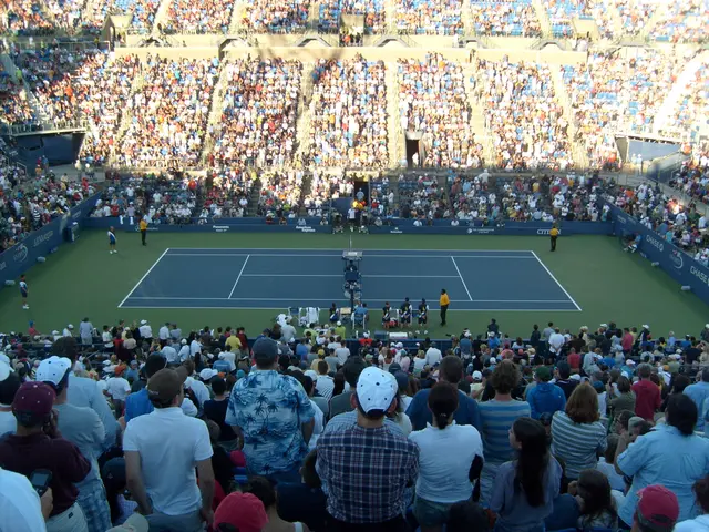 The image shows a large crowd of people watching a tennis match in a stadium. The court is filled...