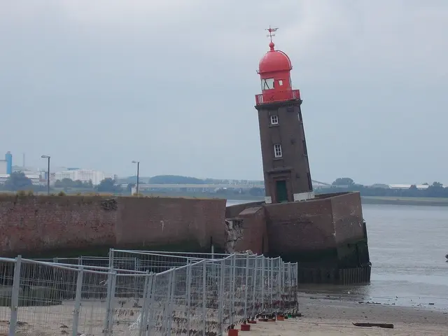 The image shows a red lighthouse sitting atop a sandy beach next to a body of water, with a boat on...