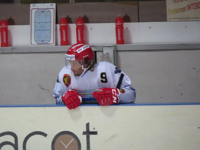 The image shows a hockey player sitting on the bench in front of a wall, wearing a helmet and...