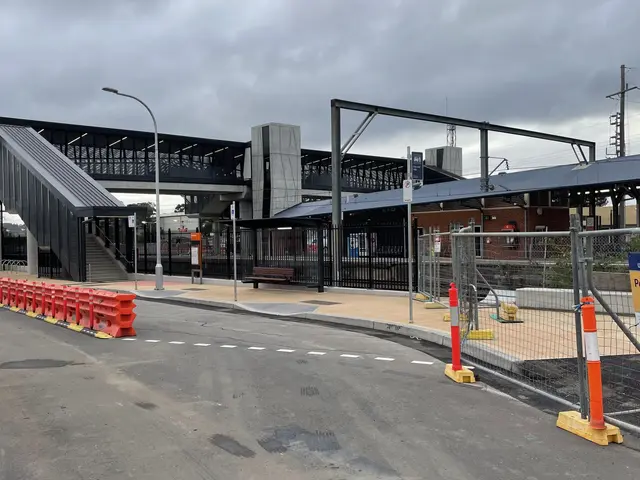 The image shows a train station with a bridge in the background, street poles, street lights,...