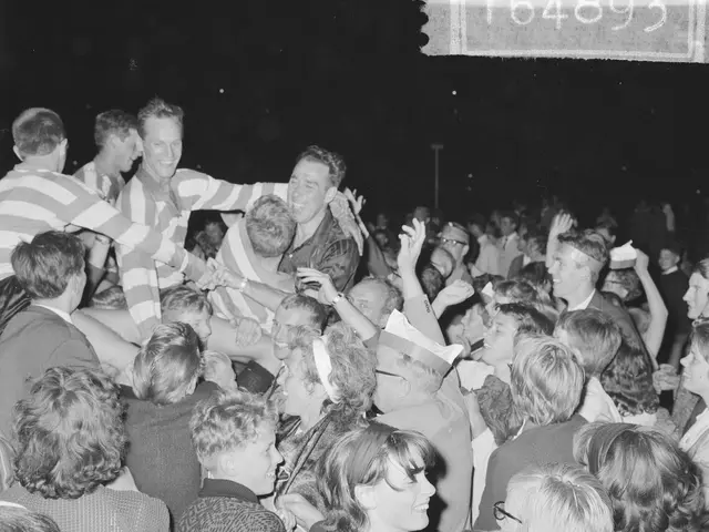 The image shows a black and white photo of a crowd of people at a concert. In the center of the...