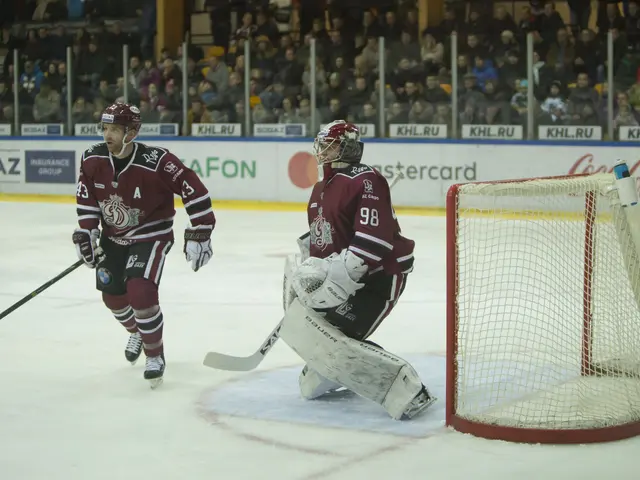 The image shows two men playing hockey on an ice rink in front of a crowd. They are both wearing...
