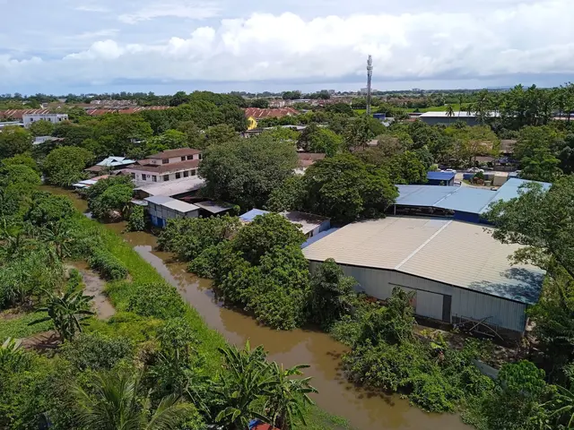 The image shows an aerial view of a small town with a river running through it, surrounded by...