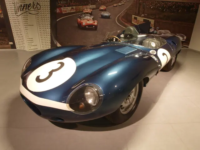 The image shows a blue and white sports car on display in a museum, surrounded by other vehicles on...