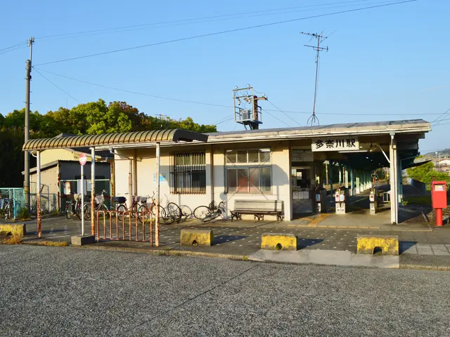 The image shows a train station with bicycles parked in front of it. There is a road at the bottom...