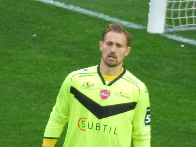 The image shows a man in a yellow goalkeeper's uniform standing on a soccer field, with a goal post...