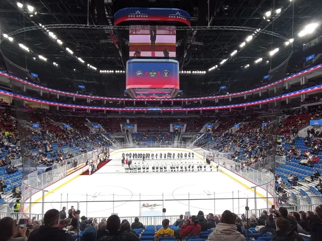 The image shows a large arena filled with lots of people watching a hockey game. In the center of...
