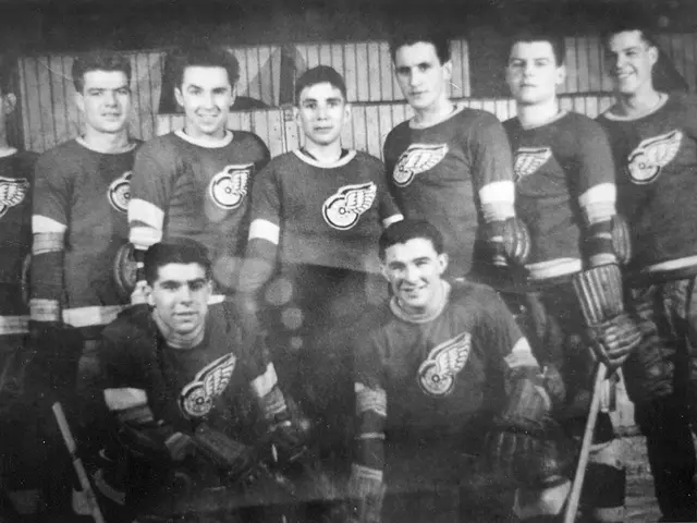 The image shows a black and white photo of a hockey team, with some of the players standing and...