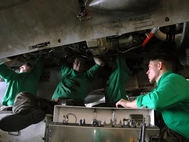 The image shows three men in green shirts working on an airplane. They are sitting on the underside...