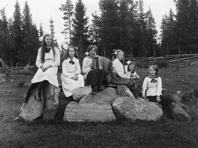 The image shows a group of young girls sitting on top of a rock in a grassy area surrounded by...