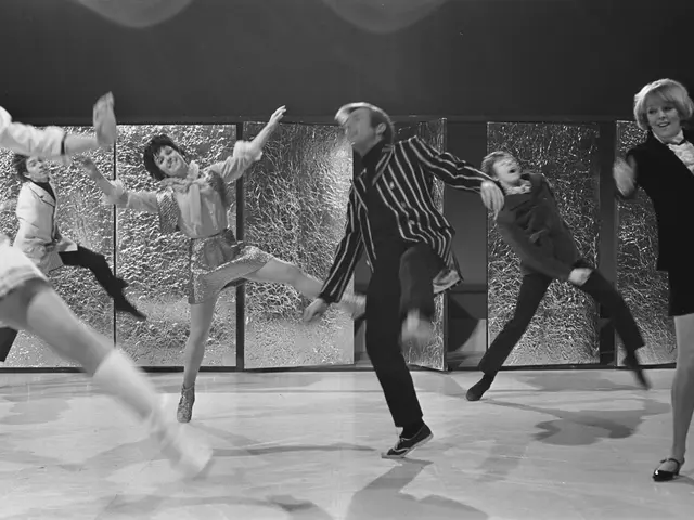 The image shows a group of people dancing on a stage, with a wall in the background. The image is...