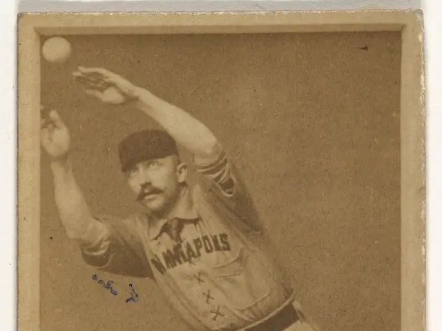 The image shows an old photo of a baseball player throwing a ball. The player is wearing a baseball...