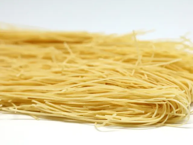 The image shows a pile of spaghetti on a white background. The noodles are a light yellow color and...