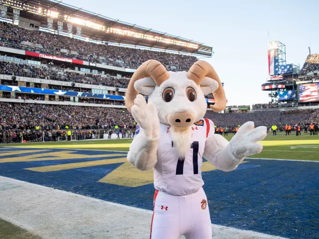 The image shows a person in a mascot costume standing on top of a football field, surrounded by a...
