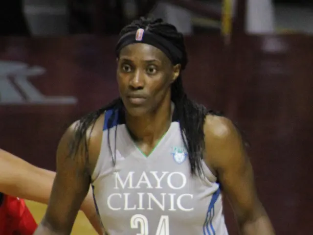 The image shows two women playing basketball on a court with a crowd of people watching. One of the...