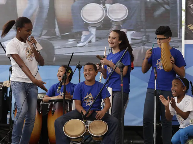 The image shows a group of children playing musical instruments on a stage, with a woman standing...
