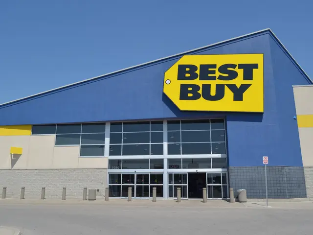 The image shows a Best Buy store front with a sign that reads "Best Buy" on it, surrounded by poles...